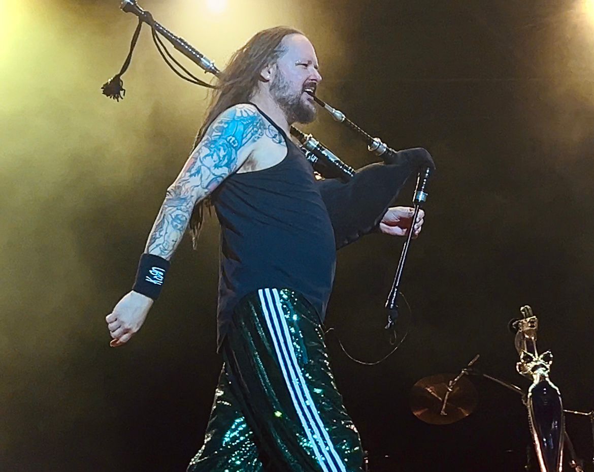 A photo of Korn frontman Jonathan Davis striding across the stage while playing the bagpipes.